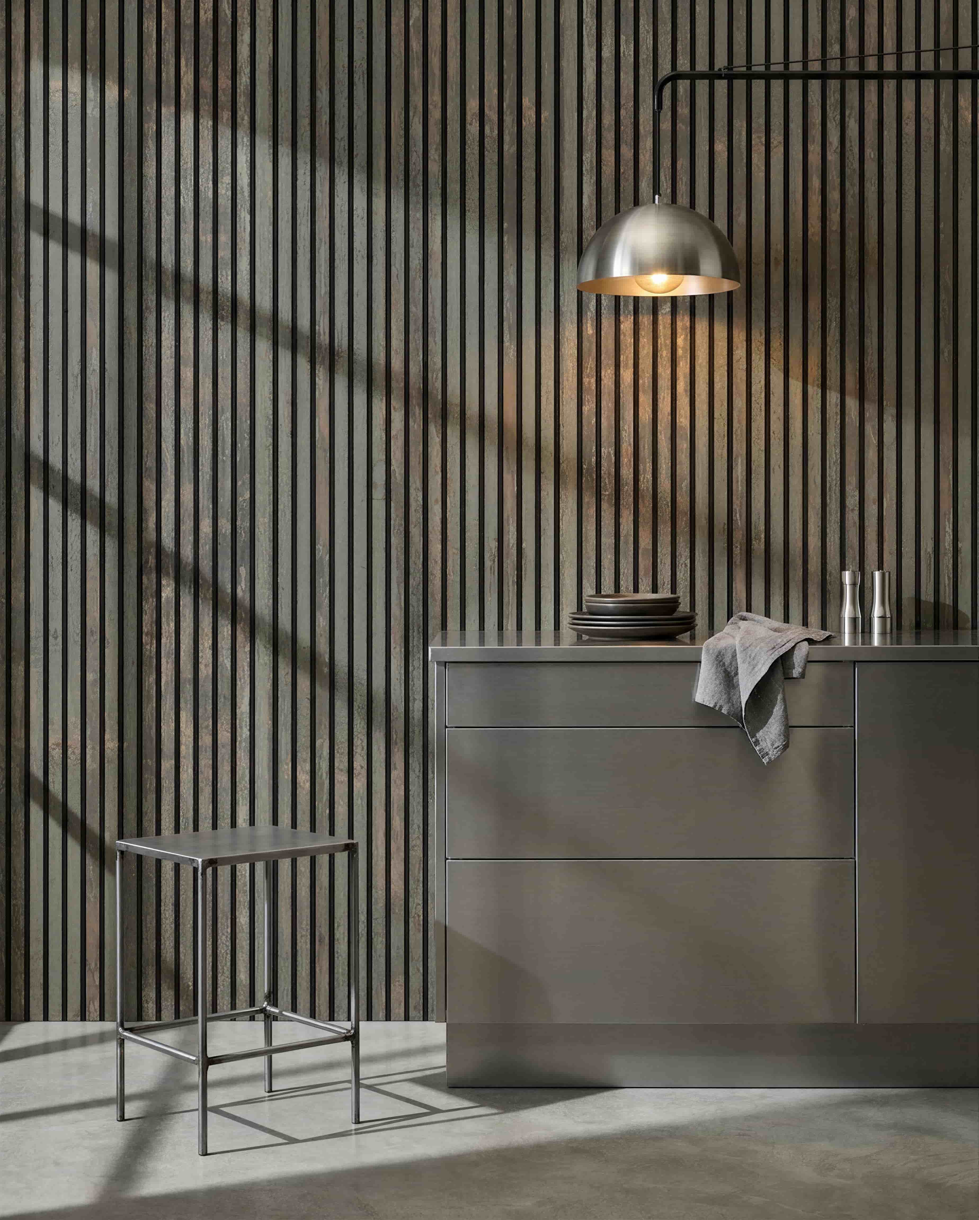 Minimalistisk køkken med metalskammel, grå ø og tallerkener, med et WoodUpp Akupanel akustisk træpanel i Oxide Grey/Black Felt til lydkontrol.